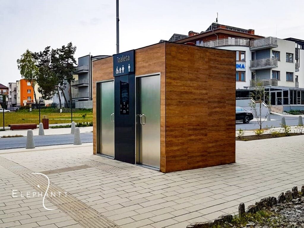 Automatyczna dwustanowiskowa prostokątna toaleta miejska City S2 w Szczecinku. Elewacja wykonana z płyt gresowych imitujących drewno